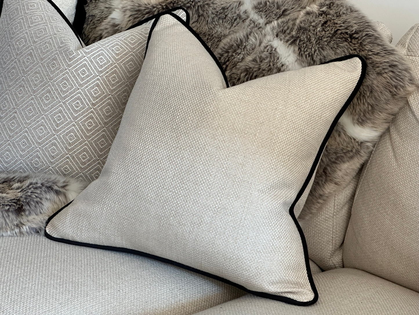 Close-up of cream cushion with contrast black piping, showing texture and trim detail.