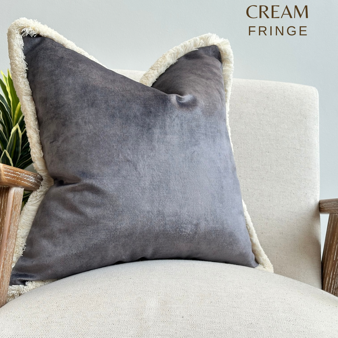 Grey velvet cushion with cream fluffy fringe trim.