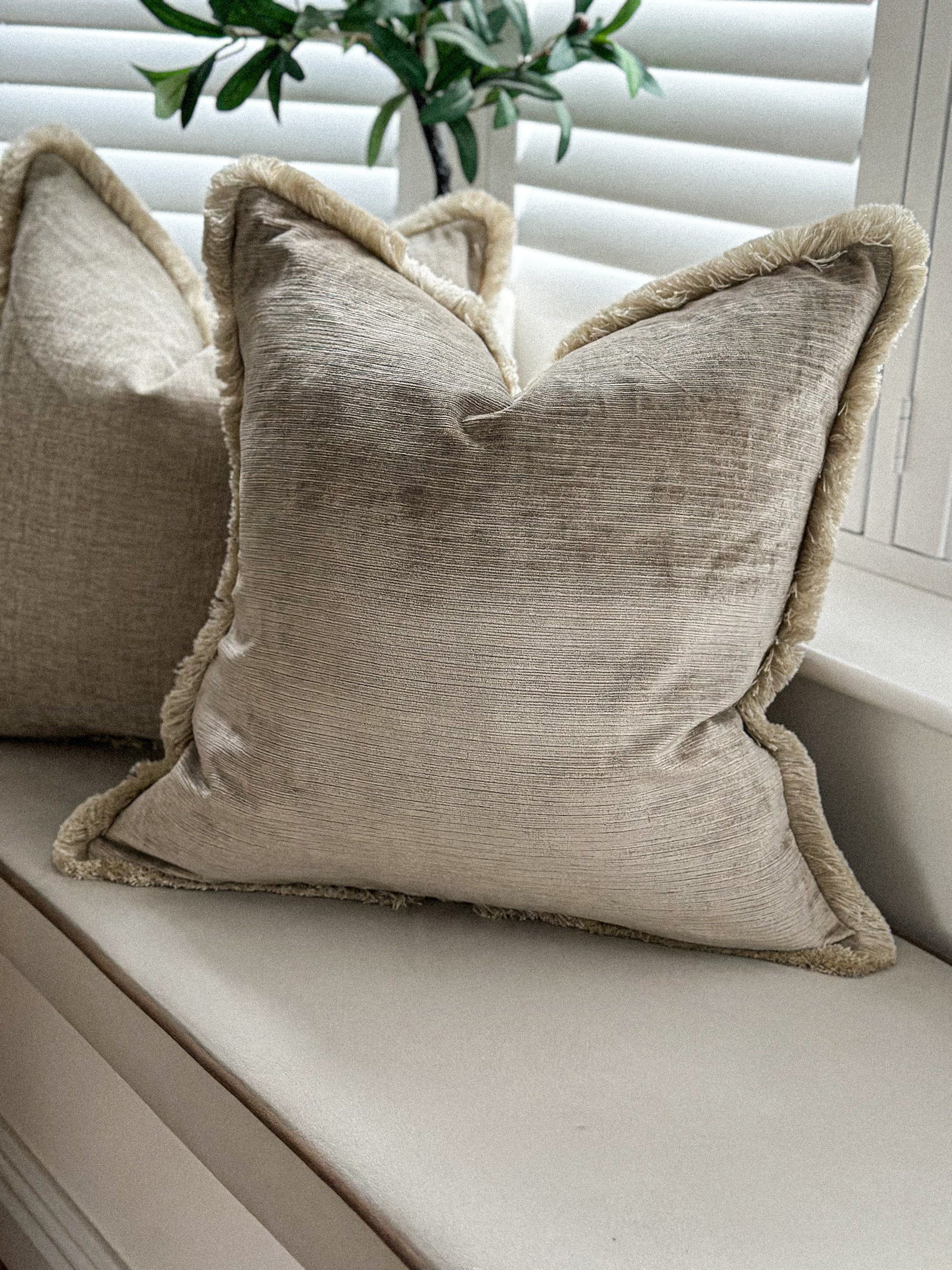 Champagne-beige velvet cushion with matching fringe styled on a neutral window seat.