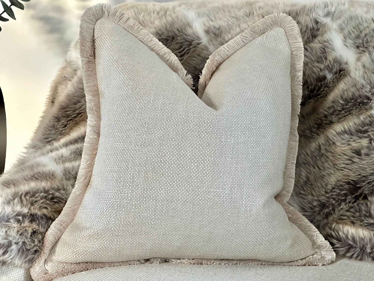Luxury bespoke cushion in an elegant warm ivory cream hue, crafted from high-end textured fabric and finished with luxurious fringe trim for that designer look.