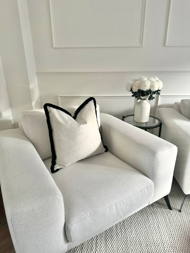 Neutral luxury cushion with black fringe trim.