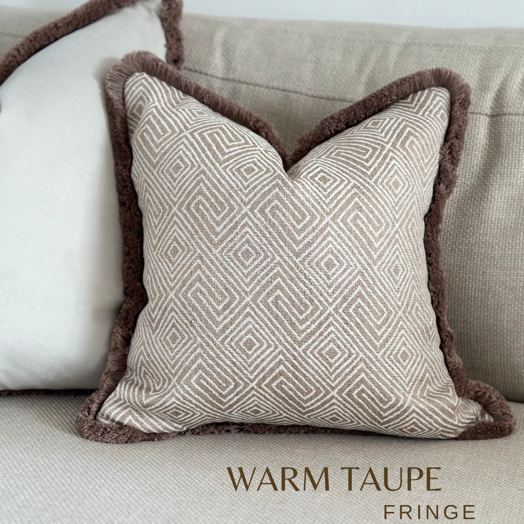 A luxury beige tan geometric cushion with fringing. Set in a Neutral Minimalistic home decor setting.