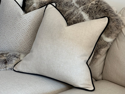 Close-up of cream cushion with contrast black piping, showing texture and trim detail.
