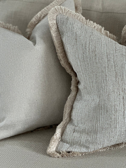 Neutral textured cushion with fluffy trim.