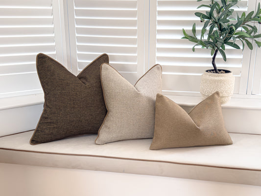 A photo of a neutral cushion combination, it includes a dark brown a textured cream and a rustic beige rectangle cushion.