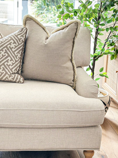 Warm beige scatter cushion with subtle texture and soft fringed edging.