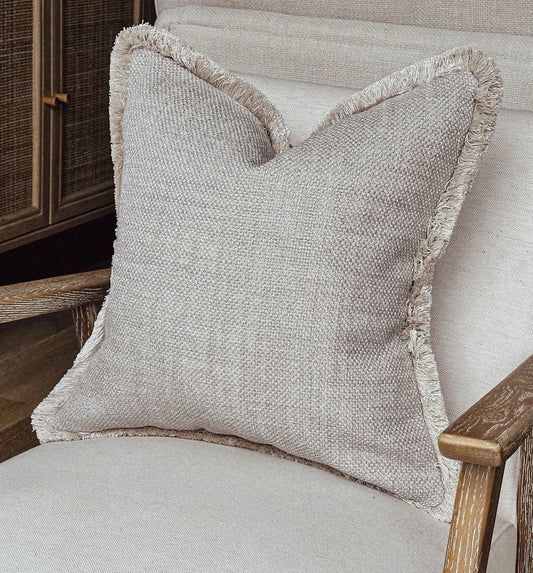 Greige textured cushion with fringe trim.