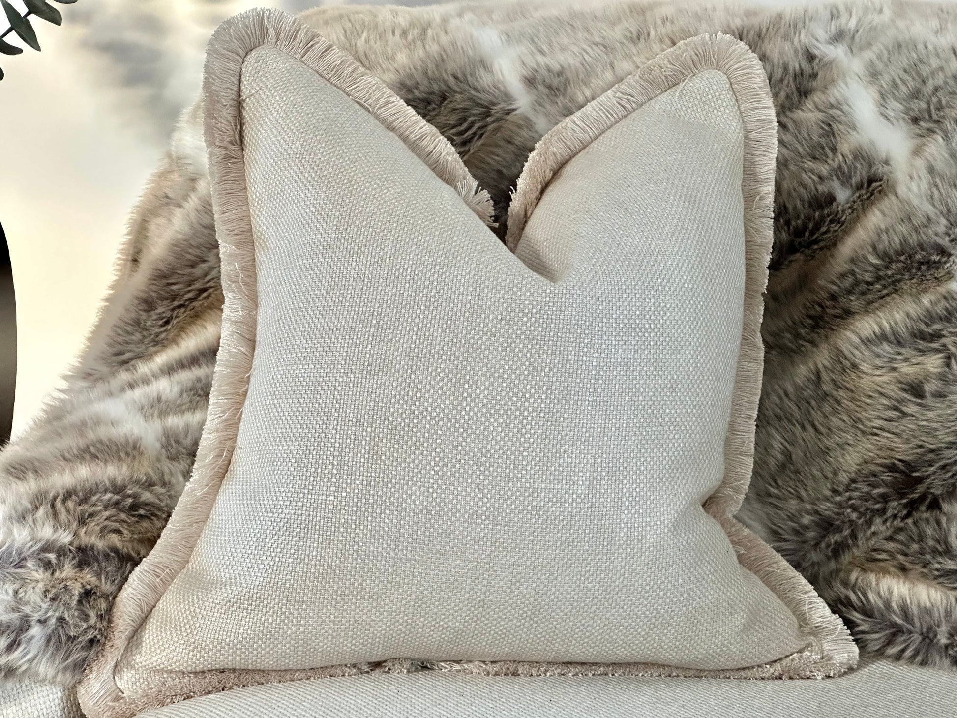 Luxury bespoke cushion in an elegant warm ivory cream hue, crafted from high-end textured fabric and finished with luxurious fringe trim for that designer look.