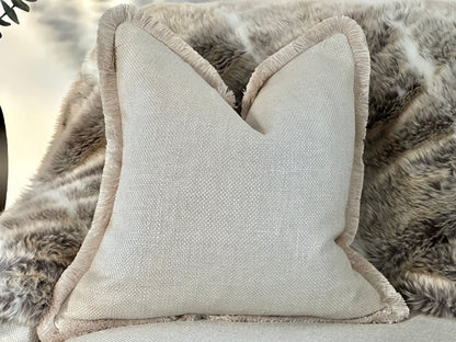 Luxury bespoke cushion in an elegant warm ivory cream hue, crafted from high-end textured fabric and finished with luxurious fringe trim for that designer look.
