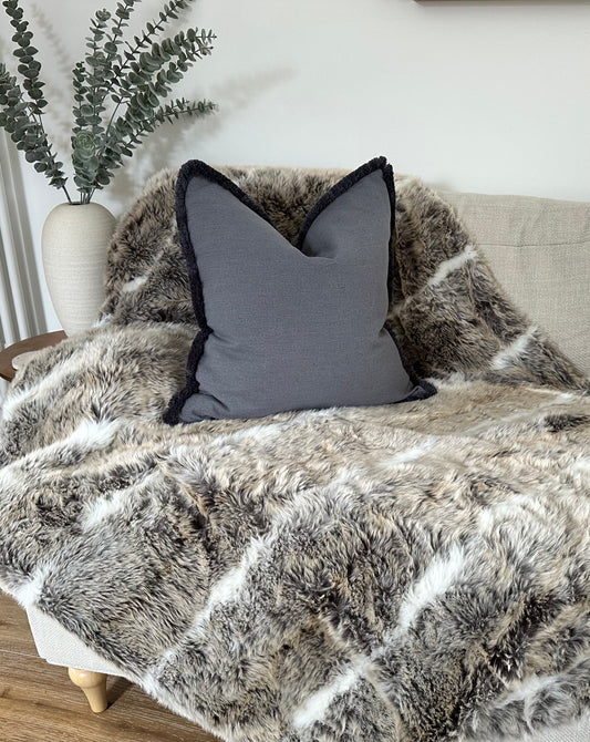 Grey blue cushion with fringe trim.