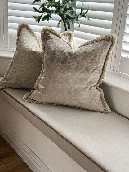 Neutral velvet scatter cushion featuring warm beige tones and fringe edging.

