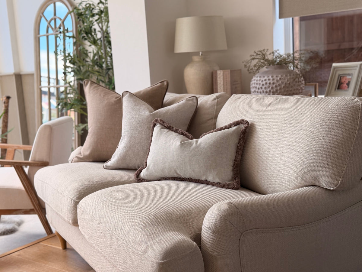 A beige upholstered loveseat sofa in a bright, modern living room, styled with multiple neutral-toned throw pillows.