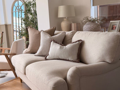 A beige upholstered loveseat sofa in a bright, modern living room, styled with multiple neutral-toned throw pillows.
