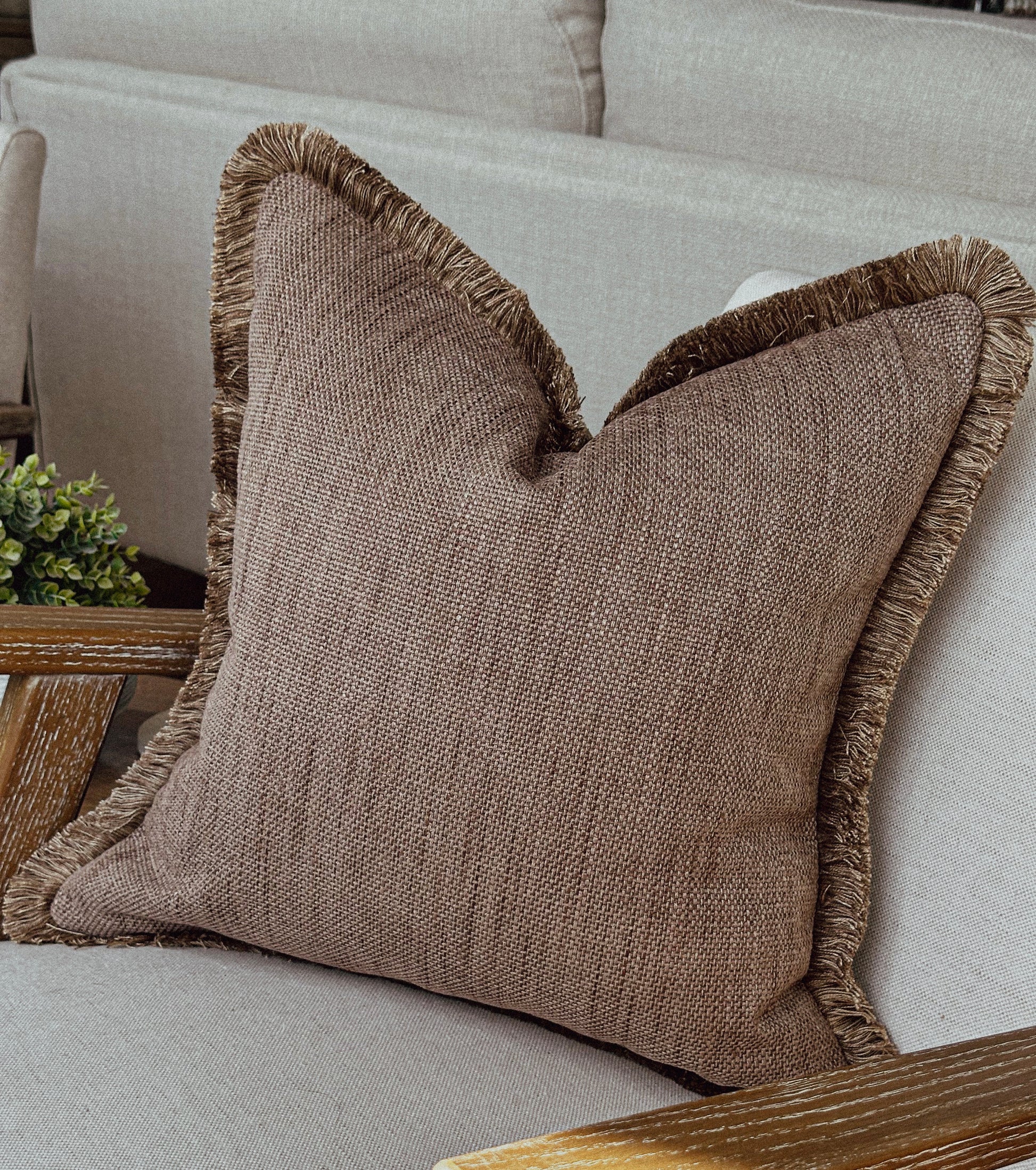 Taupe brown textured cushion with matching fringe trim styled on a neutral armchair
