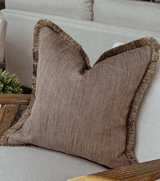 Taupe brown textured cushion with matching fringe trim styled on a neutral armchair