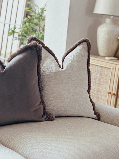 Two decorative cream pillows with brown trim on a beige sofa in a living room setting.