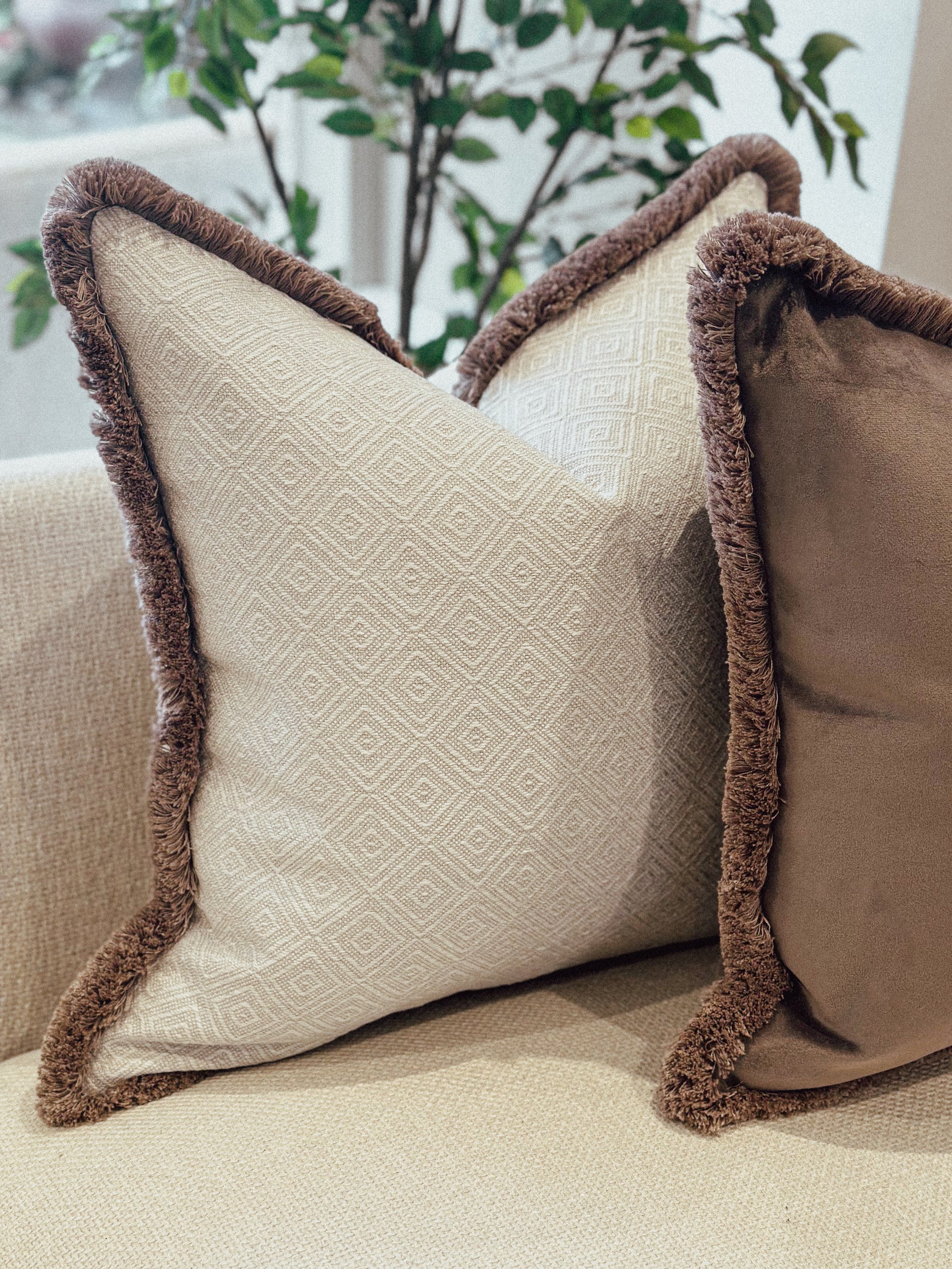 Natural geometric decorative cushion with brown trim on a beige couch.