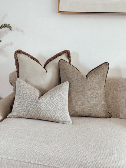 Neutral cushion combo, ivory velvet with beige fringe, textured beige cushion and a cream geometric rectangle pillow.