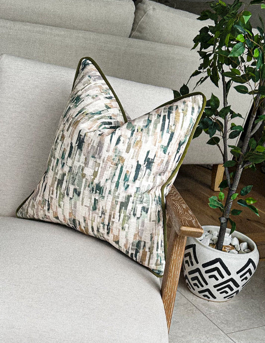 Painterly sage green and sand cushion with piped trim on a neutral chair