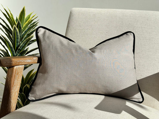 Grey linen cushion with black piping trim.
