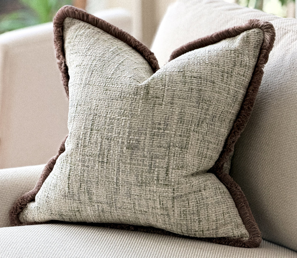 Ivory cushion with green woven texture and a fringe trim.