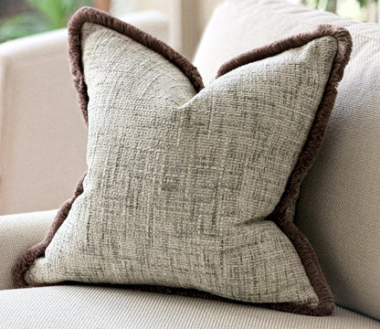 Ivory cushion with green woven texture and a fringe trim.