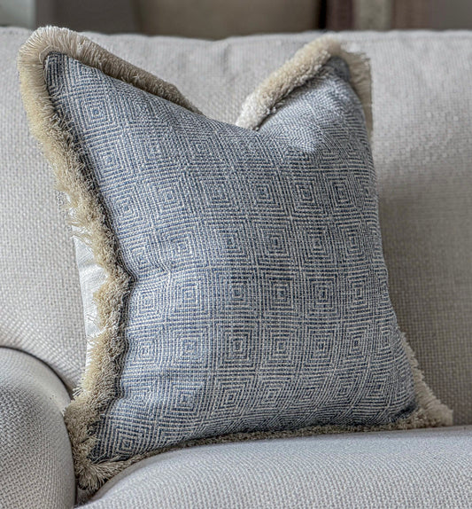 A luxury Costal blue cushion that has a geometric pattern and a fringe trim.