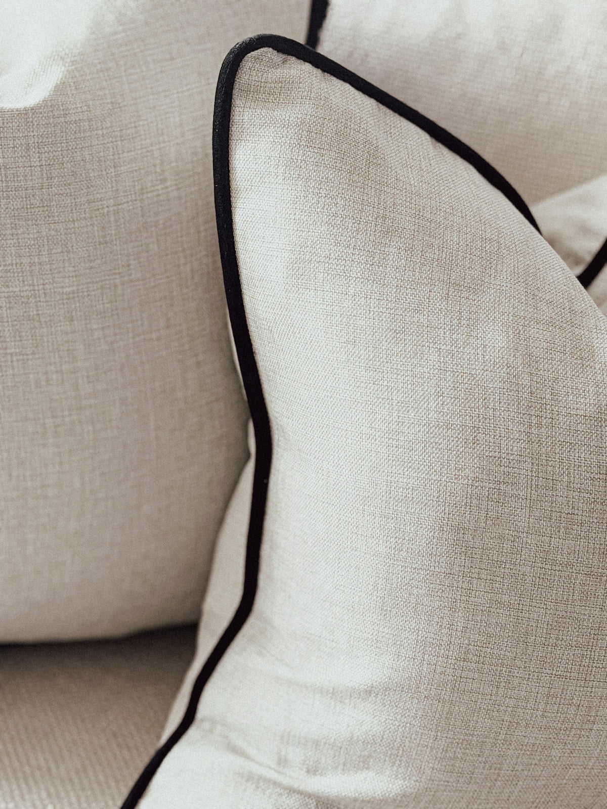 Neutral linen like fabric cushion with black edges.