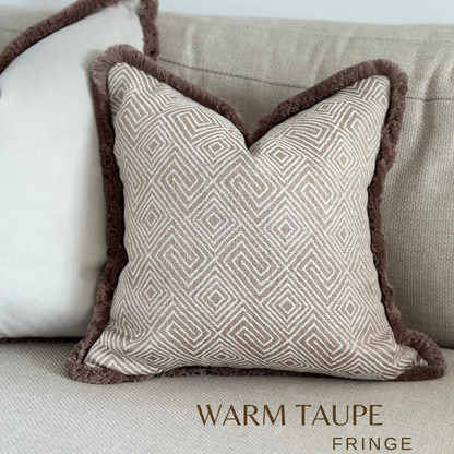 A luxury beige tan geometric cushion with fringing.  Set in a Neutral Minimalistic home decor setting. 